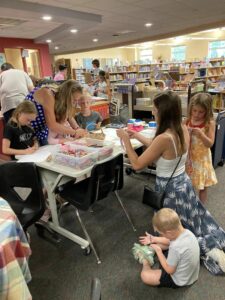 Adults help children create friendship bracelets in the library.