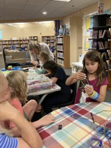 Children in a library making bracelets out of cord.