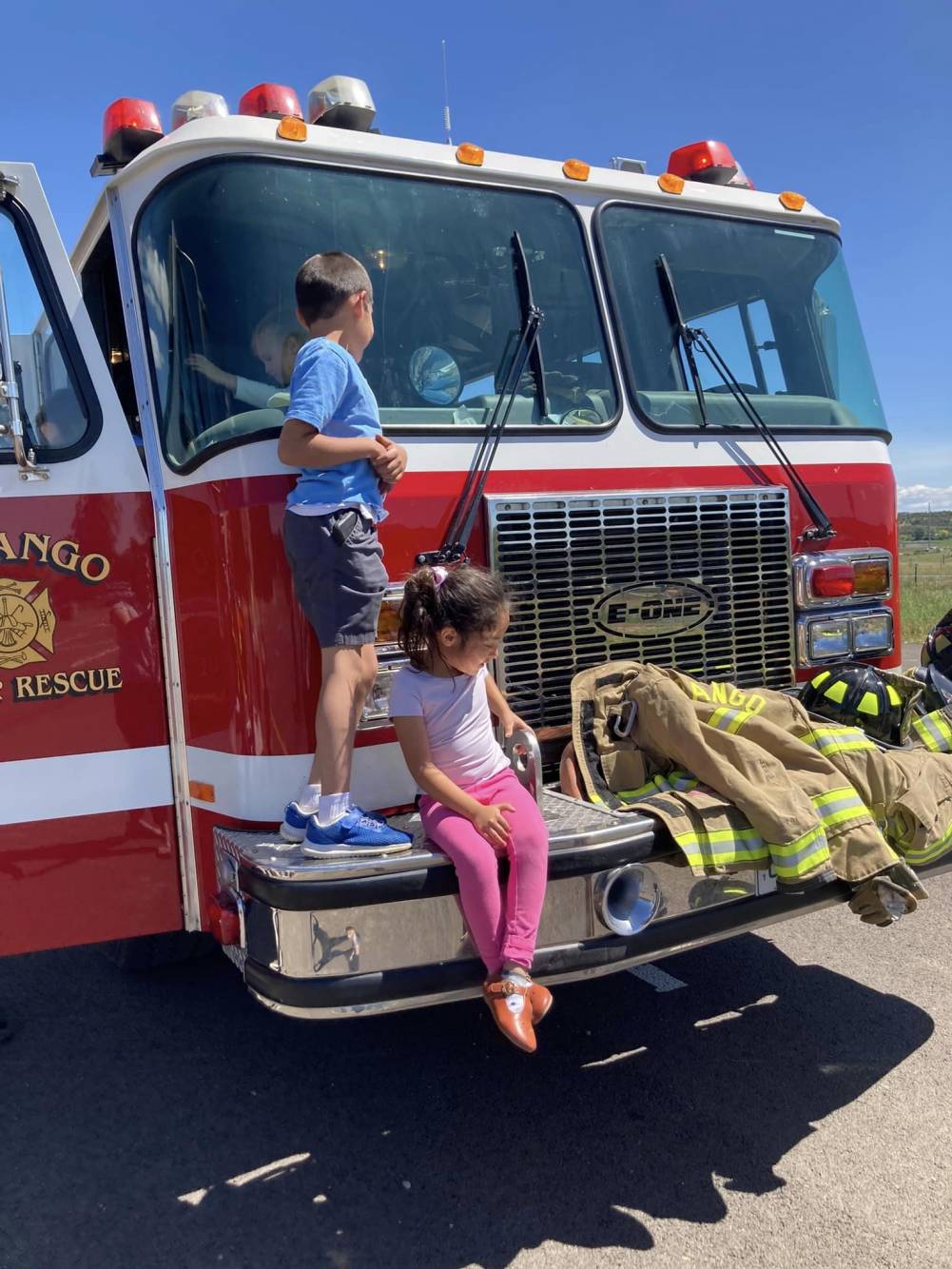 two small children climb on the bumper of a firetruck.