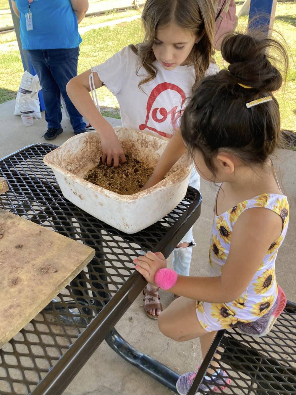 2 young girls mix seeds and soil in a plastic tub.